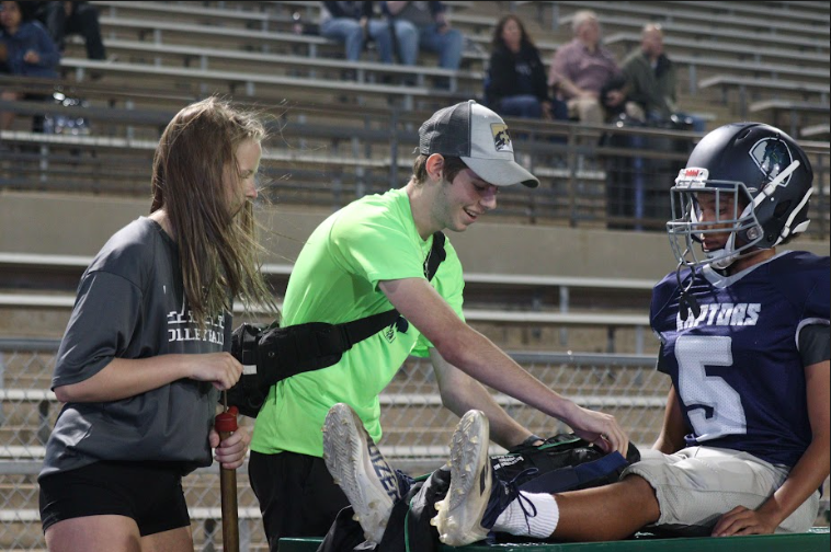 A HELPING HAND: Sports med students Sophomore Abby Aardema and Senior Adam Reisman practice their medical skills at a football game. They assist an injured player onto a stretcher while tending to their leg. photo by Isha Sheth
