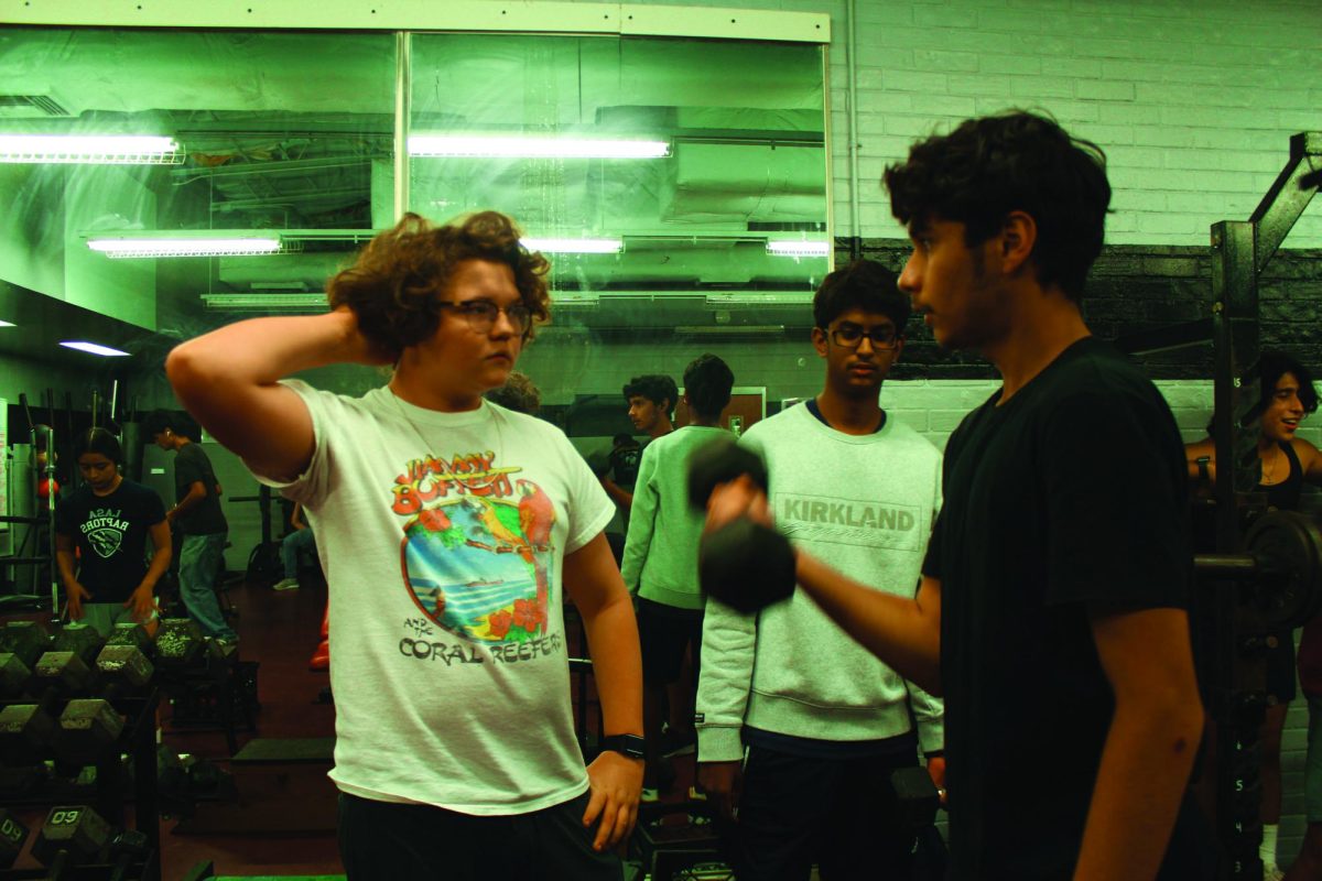WATCH AND OBSERVE | Photo editor, Griffin Beam, learns how to do a bicep curl during lifting club. Sophomore and club member Jose Gonzalez assisted Beam throughout his workout.