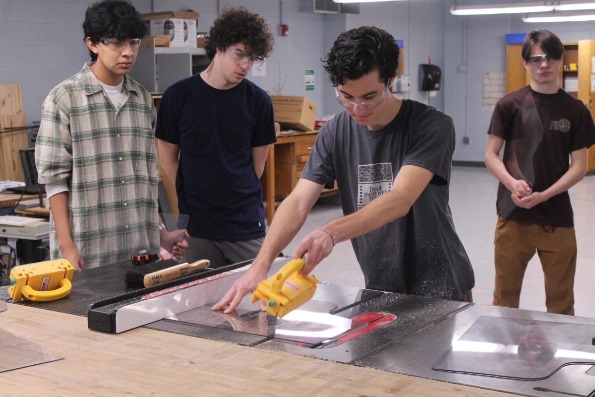 Junior Corry Grodek readies the table saw while seniors Jacinto Noriega (left), Henry Thompson (center), and Sol Garcia (right) look on.