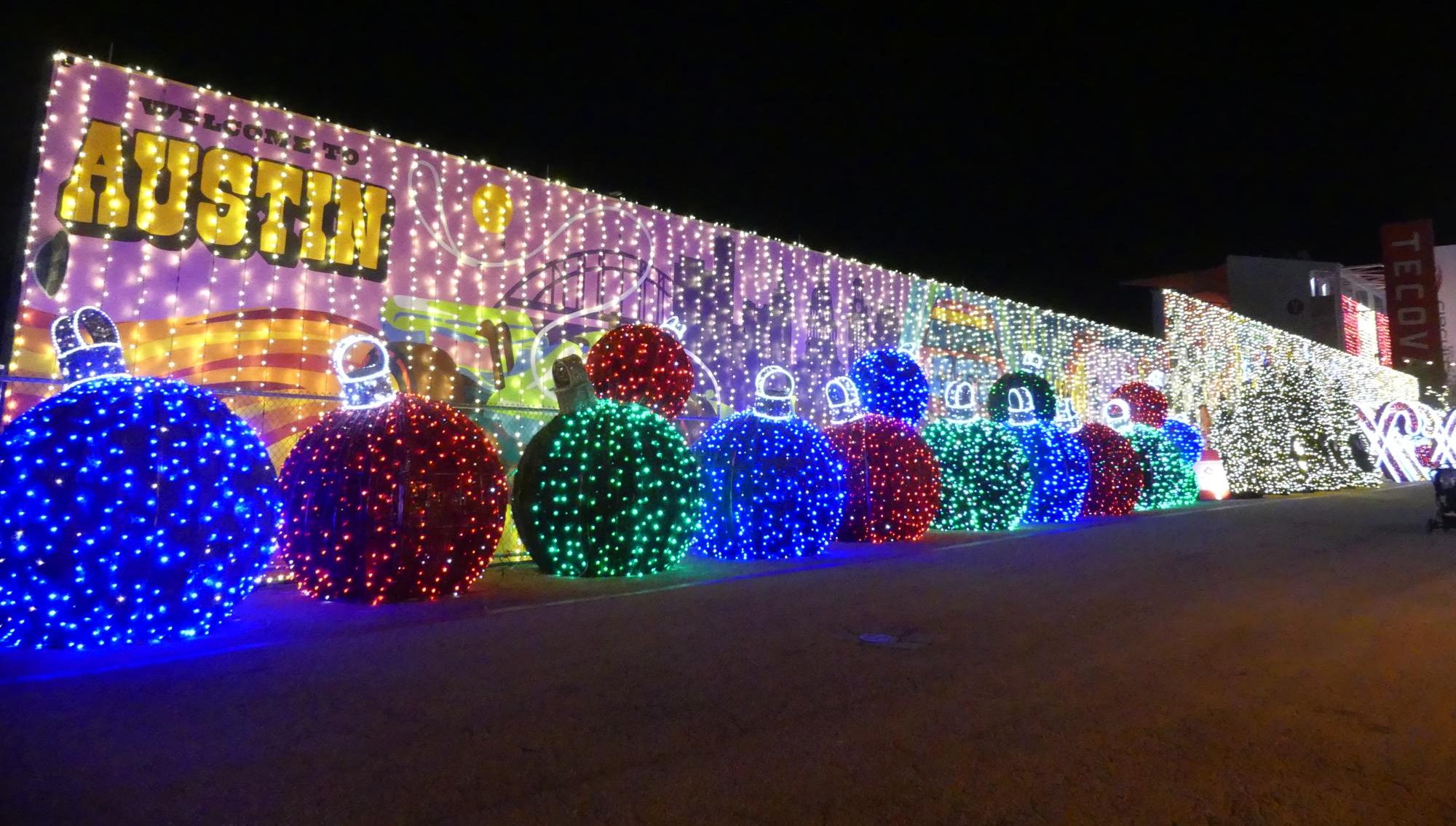 PEPPERMINT PARKWAY ENTRANCE Lights along the pathway into Circuit of The America. Ornament
bulbs lit up with many lights and signs surrounding them.